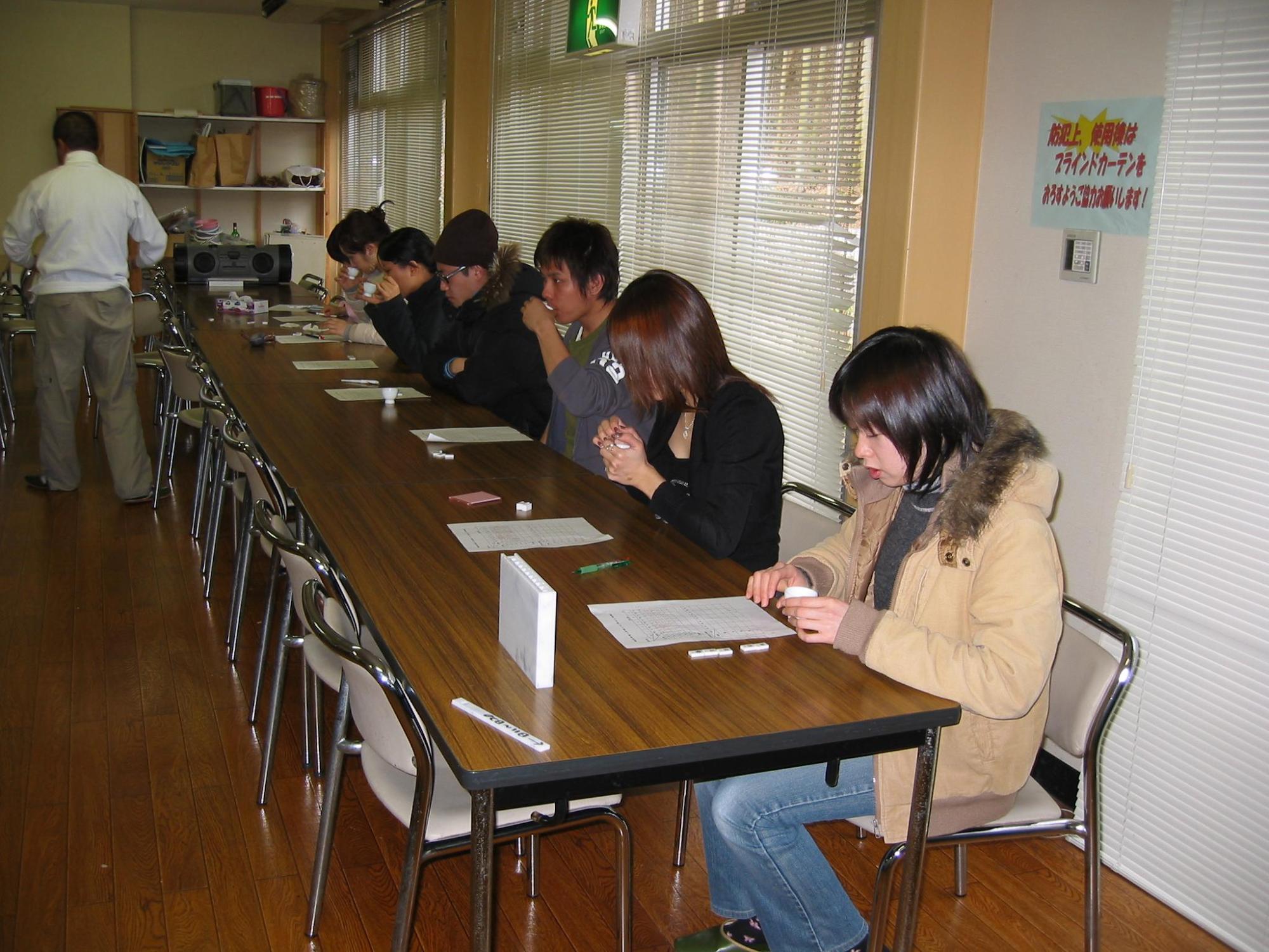 長机の席に座った男女がお茶を飲んだり、机に置かれた用紙を見ている写真