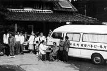 民家の前に健康パトロールカーが1台停まっており、住民が集まっている白黒写真