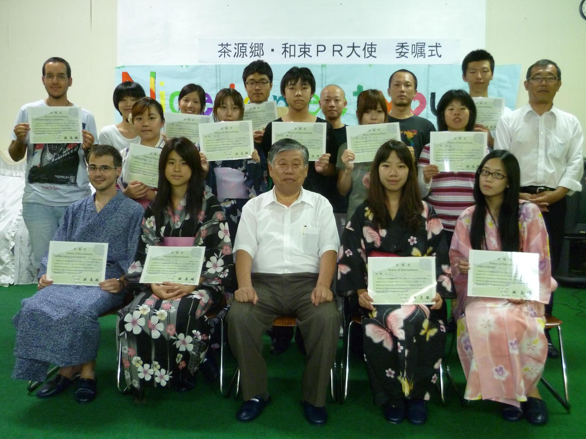 第1号の茶源郷・和束PR大使として委嘱した13名が委嘱書を持ち、町長やスタッフと一緒に記念撮影をしている写真