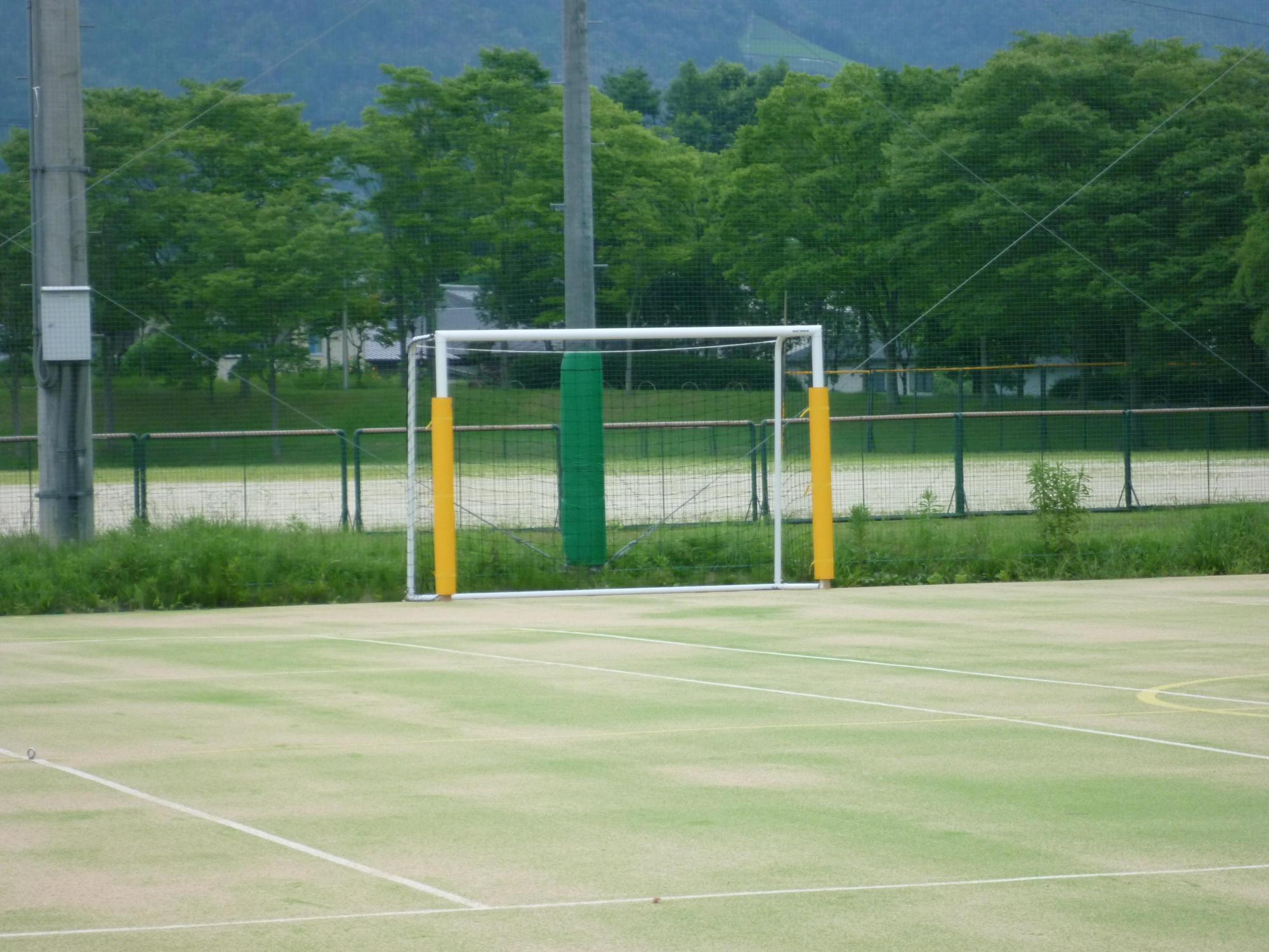 高いフェンスの手前に設置されたゴールポストとフットサルコートの写真