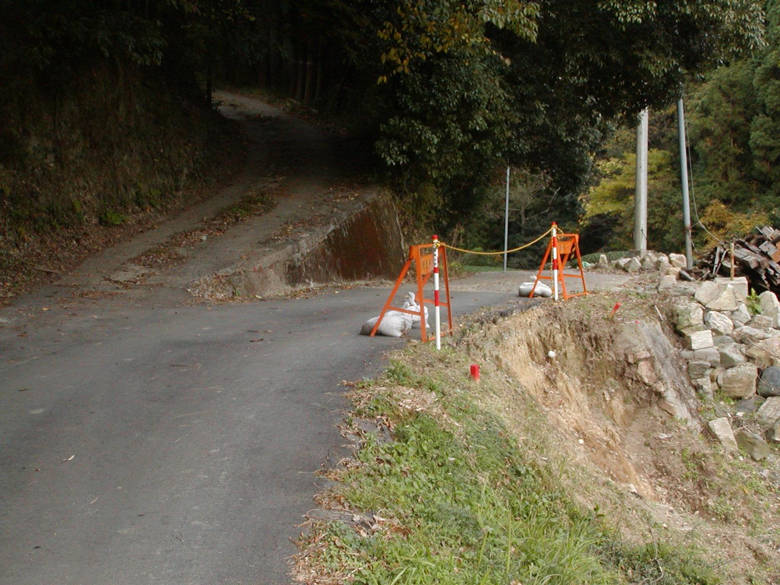 町道原山線の路肩崩壊箇所にオレンジ色のバリケードと土嚢が置いてある写真