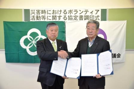 町長と吉田会長がそれぞれ協定書を開いて持ち握手をしている写真
