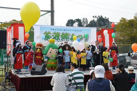 茶源郷まつりと書かれた横断幕のあるステージの上にキャラクターの着ぐるみや子供たちが立っている写真