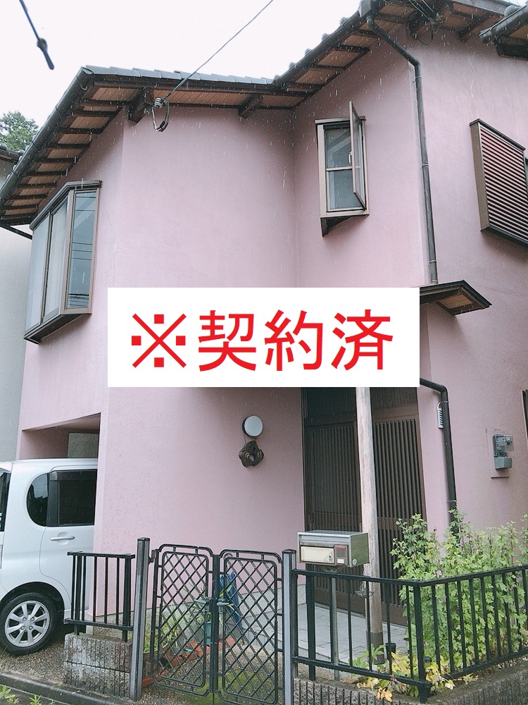 車を入れるスペースのあるピンク色の外壁の二階建ての家の写真